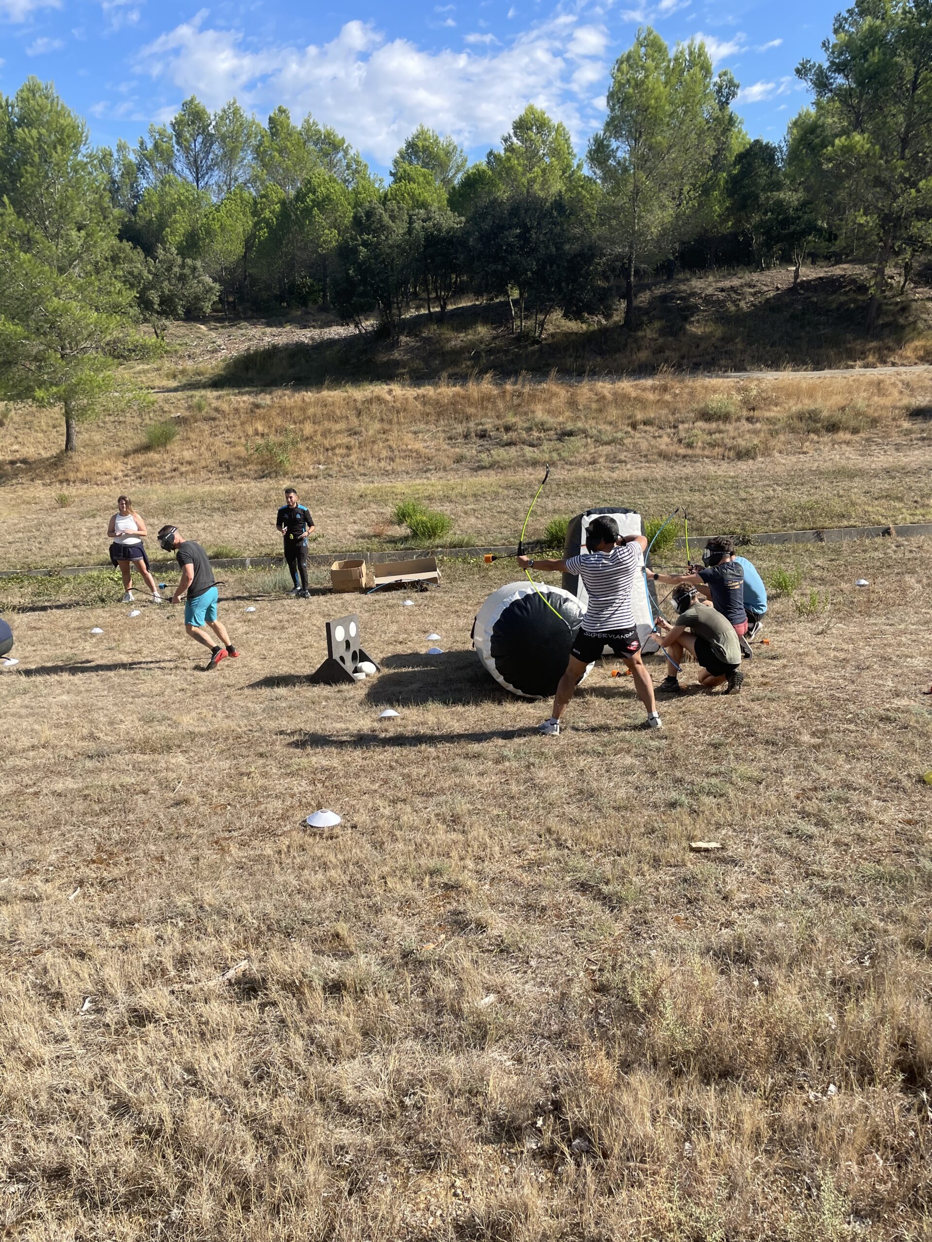 Instantané d’une compétition d’Archery Tag avec plusieurs joueurs actifs, sous un ciel bleu et en pleine nature.