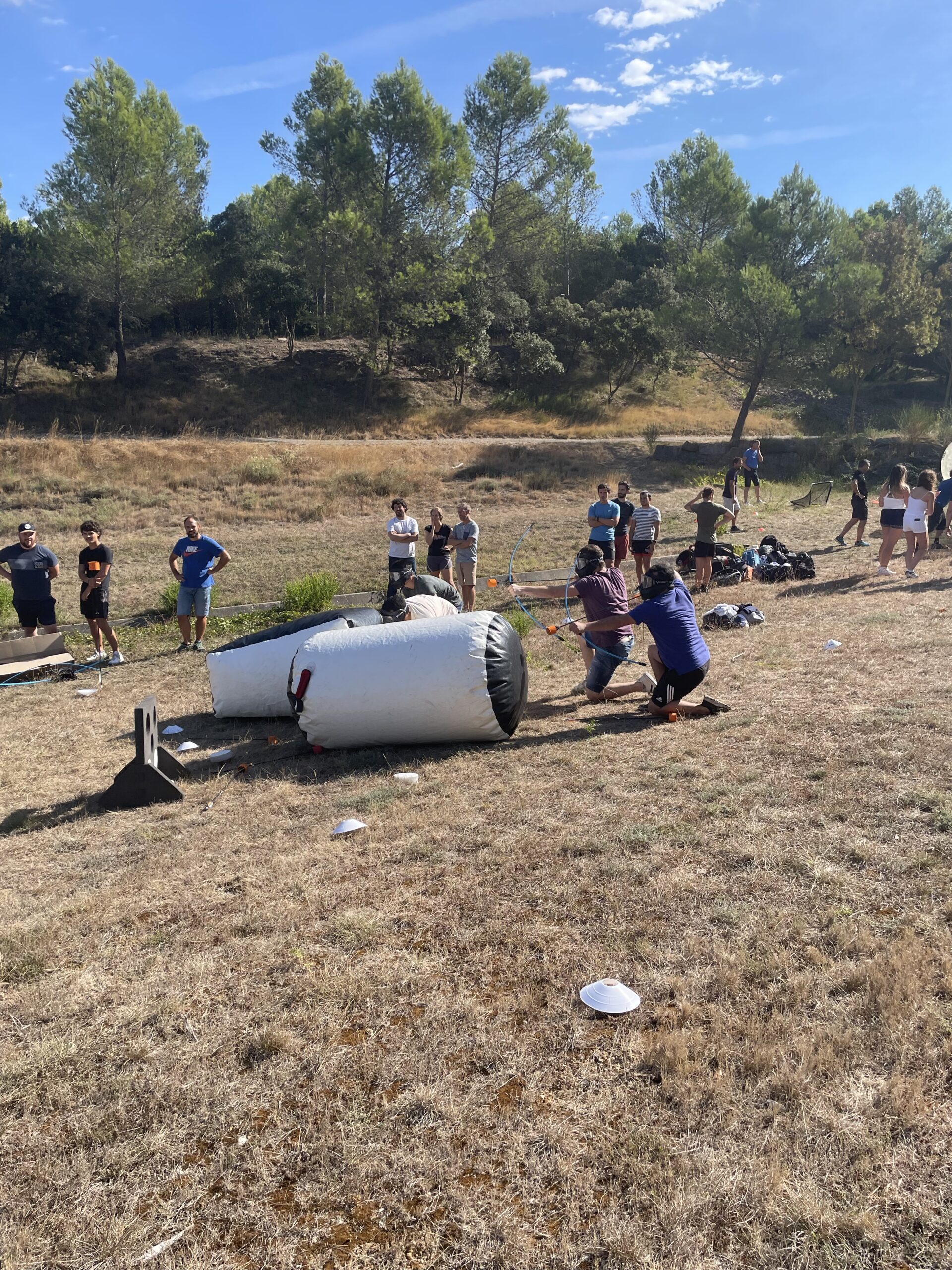 Participants en pleine partie d’Archery Tag, concentrés sur leurs tirs, dans un décor naturel avec des obstacles gonflables.