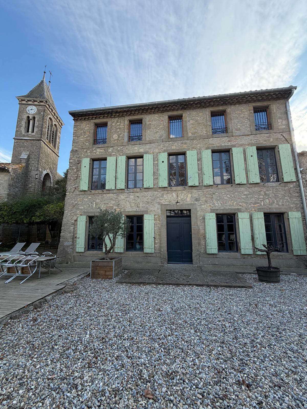 Maison en pierre avec volets verts et clocher.